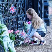 A young girl lays a floral tribute outside the Sandringham Estate