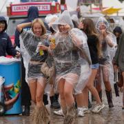 Festivalgoers shelter from the rain in plastic ponchos as they walk through the muddy site at the Reading Festival (Jeff Moore/PA)